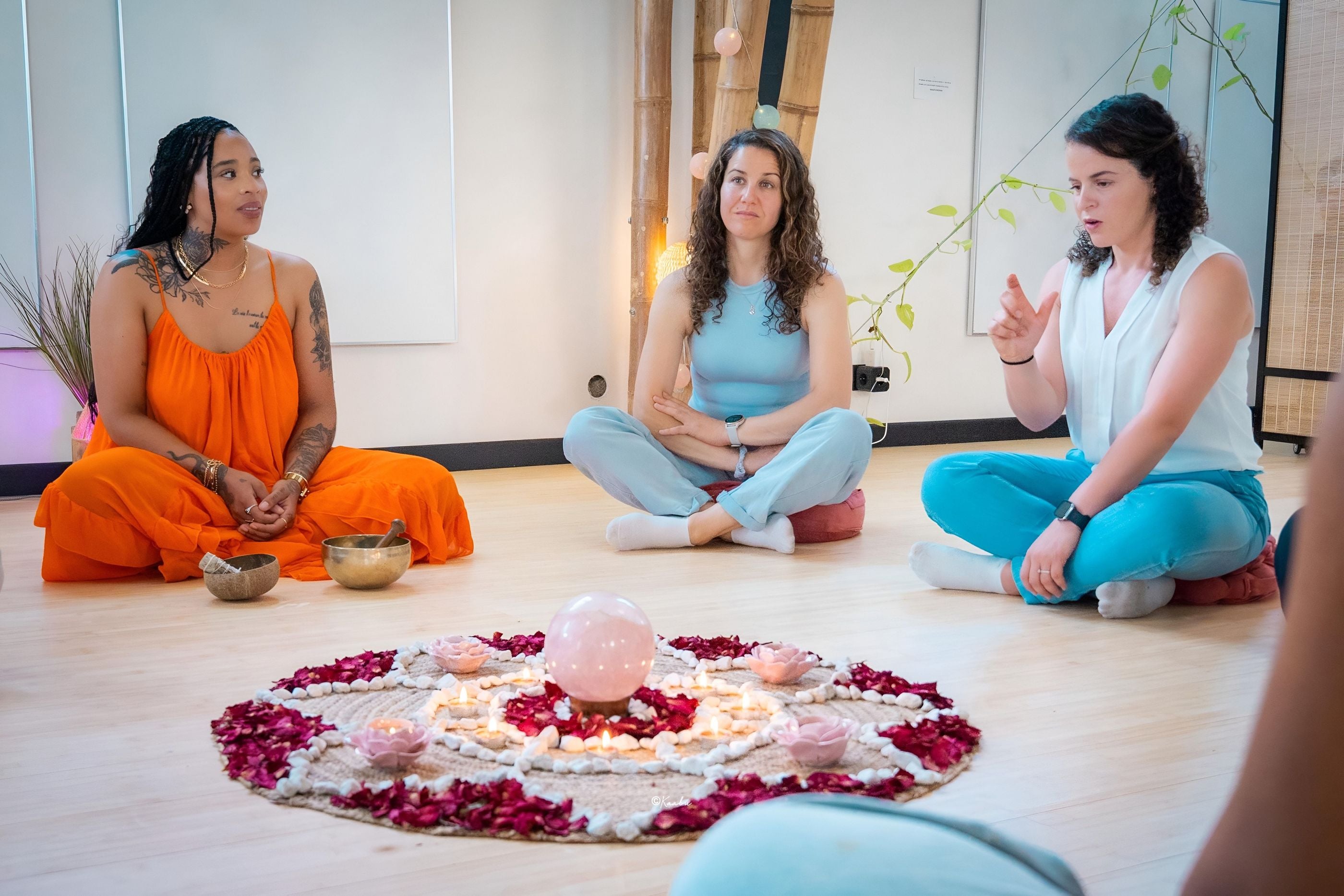 Trois femmes assises en tailleur autour d’un mandala de fleurs et de bougies