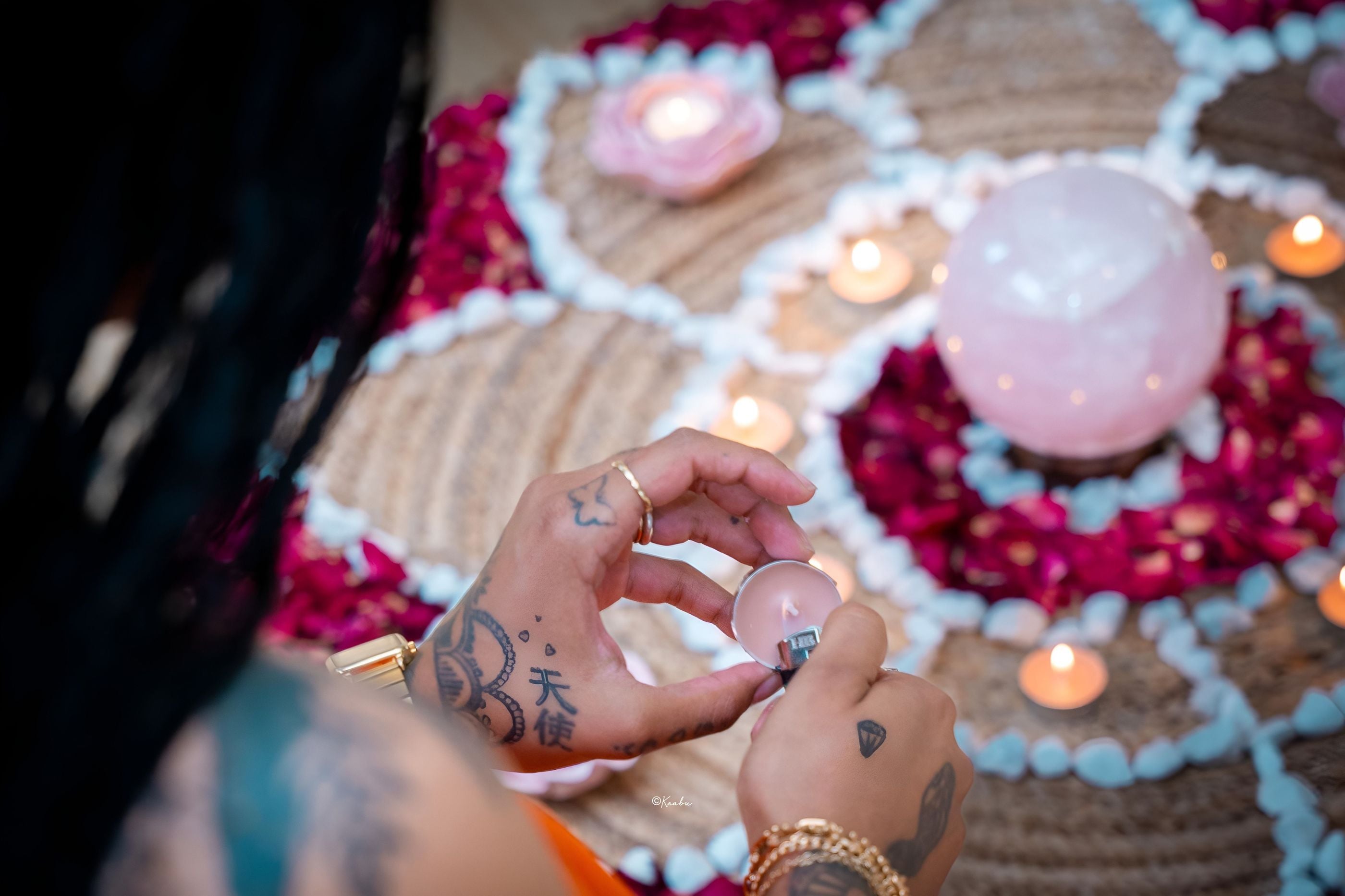 Une main au-dessus d’un mandala de pétales, de bougies et d’une sphère de quartz rose