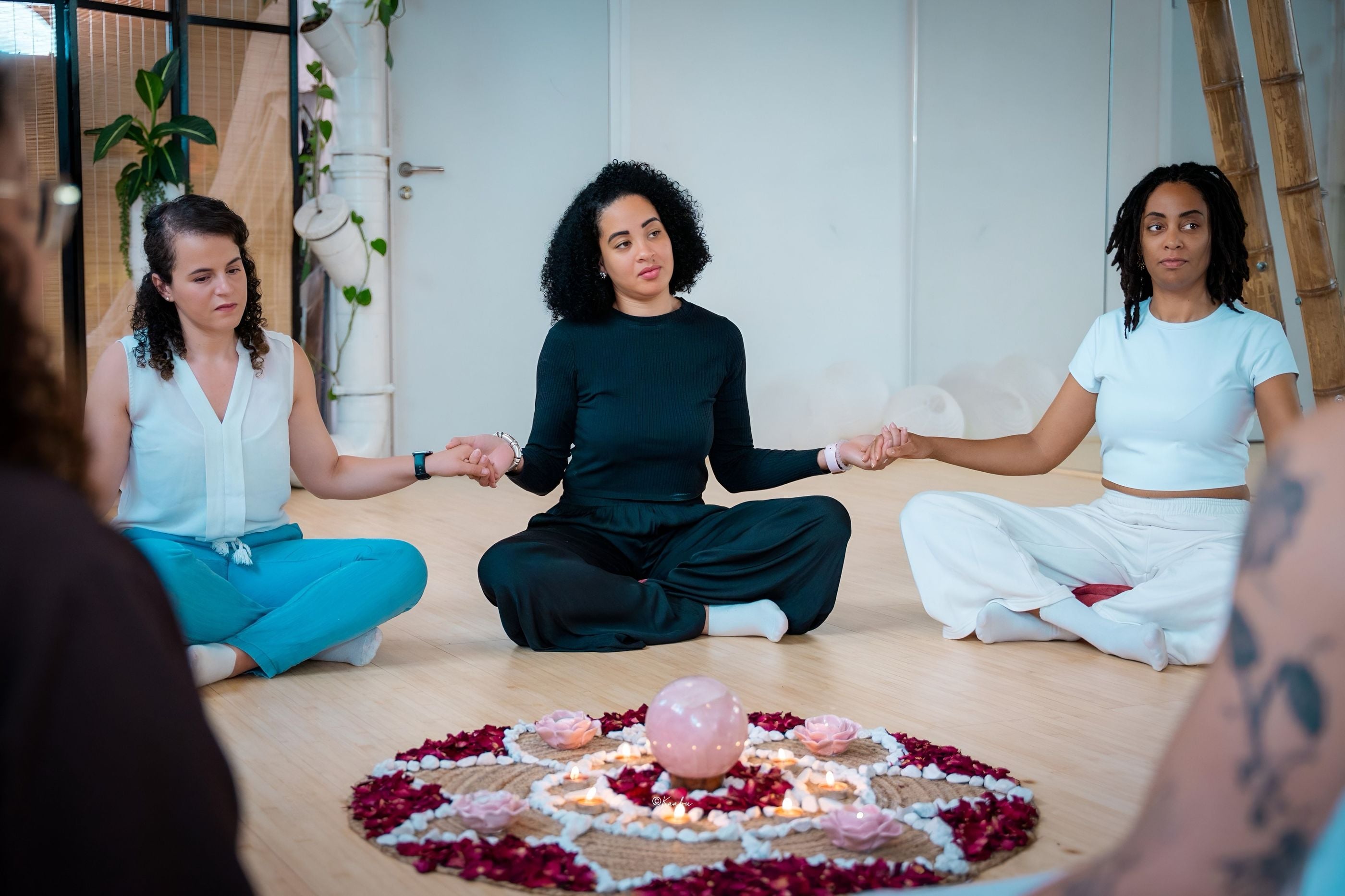 Des femmes assises en cercle se tiennent la main autour d’un mandala de fleurs