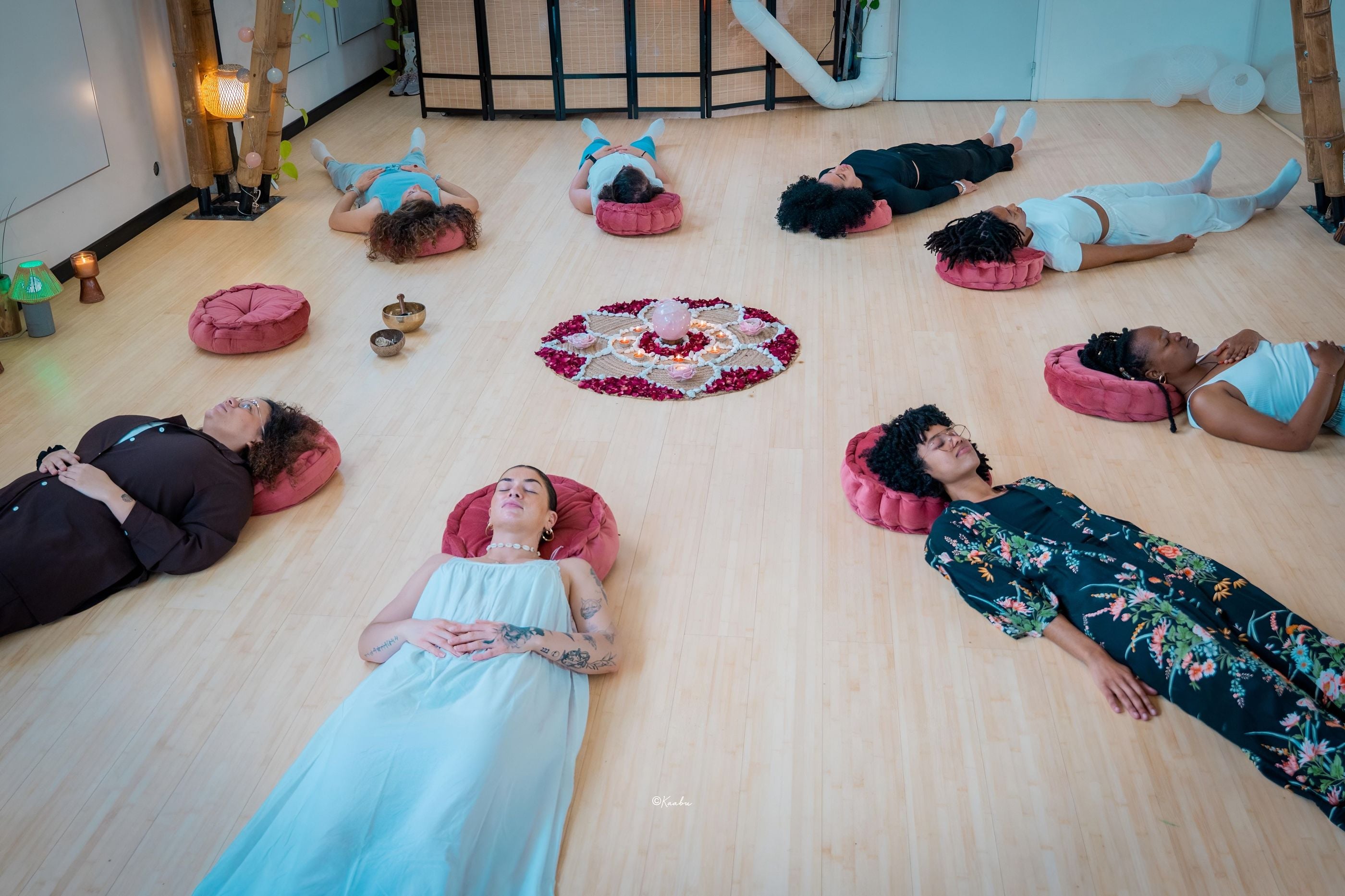 Des femmes allongées sur des coussins roses autour d’un mandala de fleurs