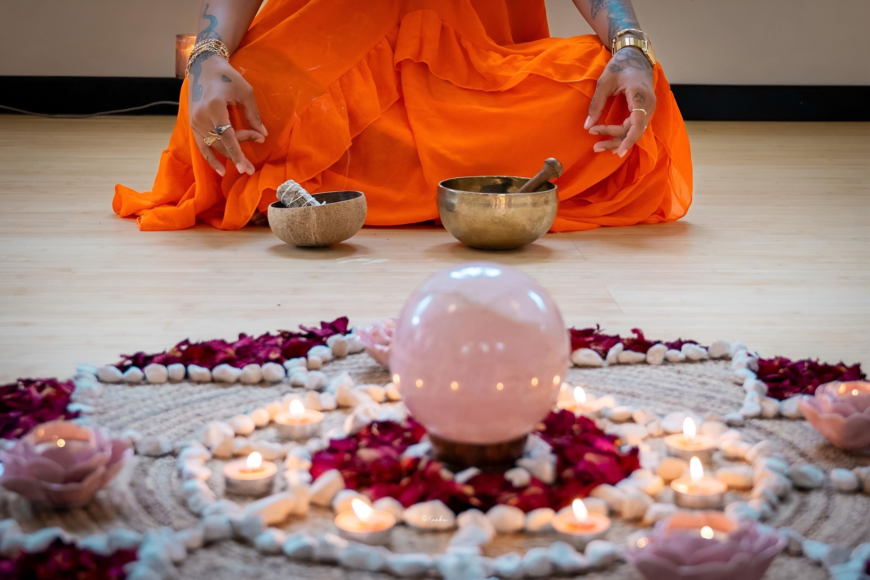 Des bols chantants et des bougies autour d’une sphère de quartz rose, sur un mandala de pétales